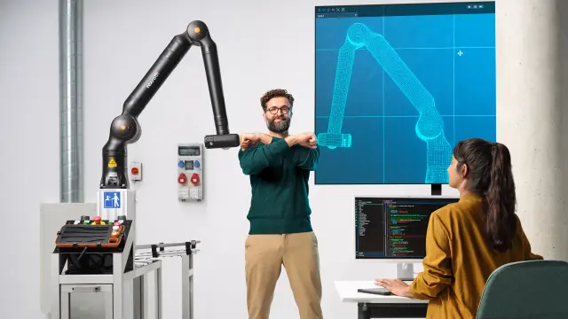 Doi asociați se joacă la o masă de fotbal cu un robot de asistență Bosch Rexroth APAS.